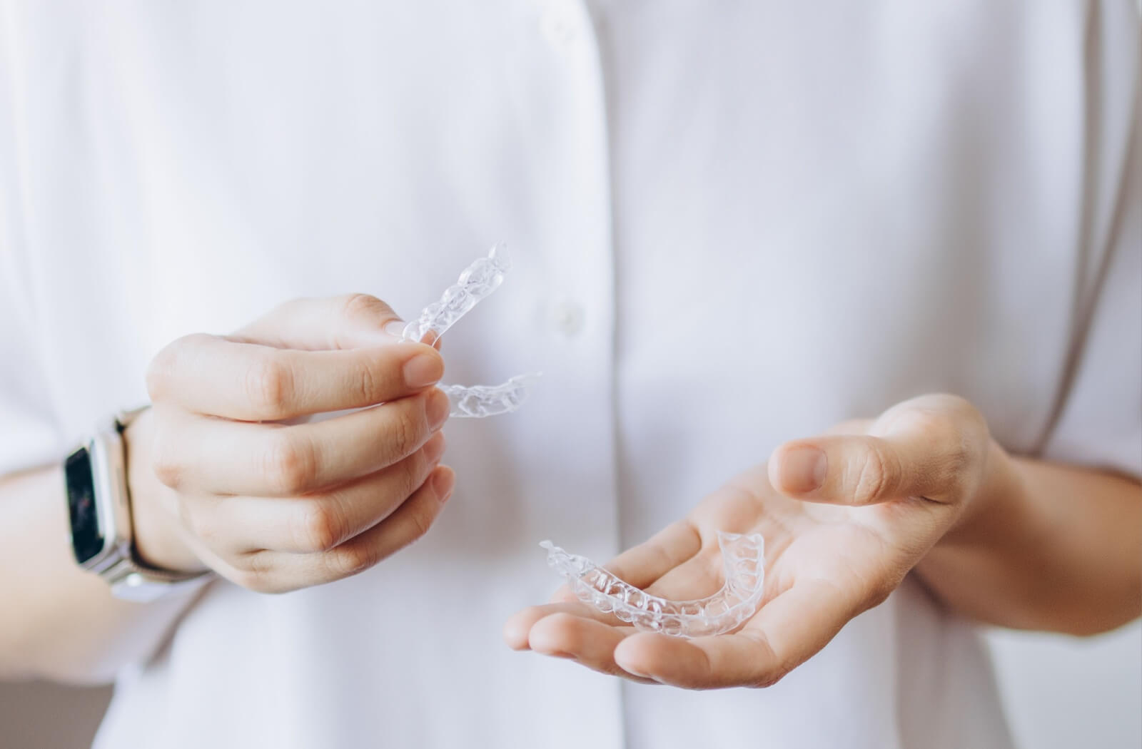 Close-up of a person holding two clear aligners, with a focus on their hands and the transparent dental devices against a plain background